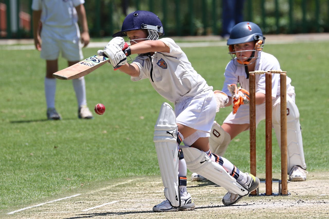 Young cricketers playing with focus and skill on a sunny outdoor field.